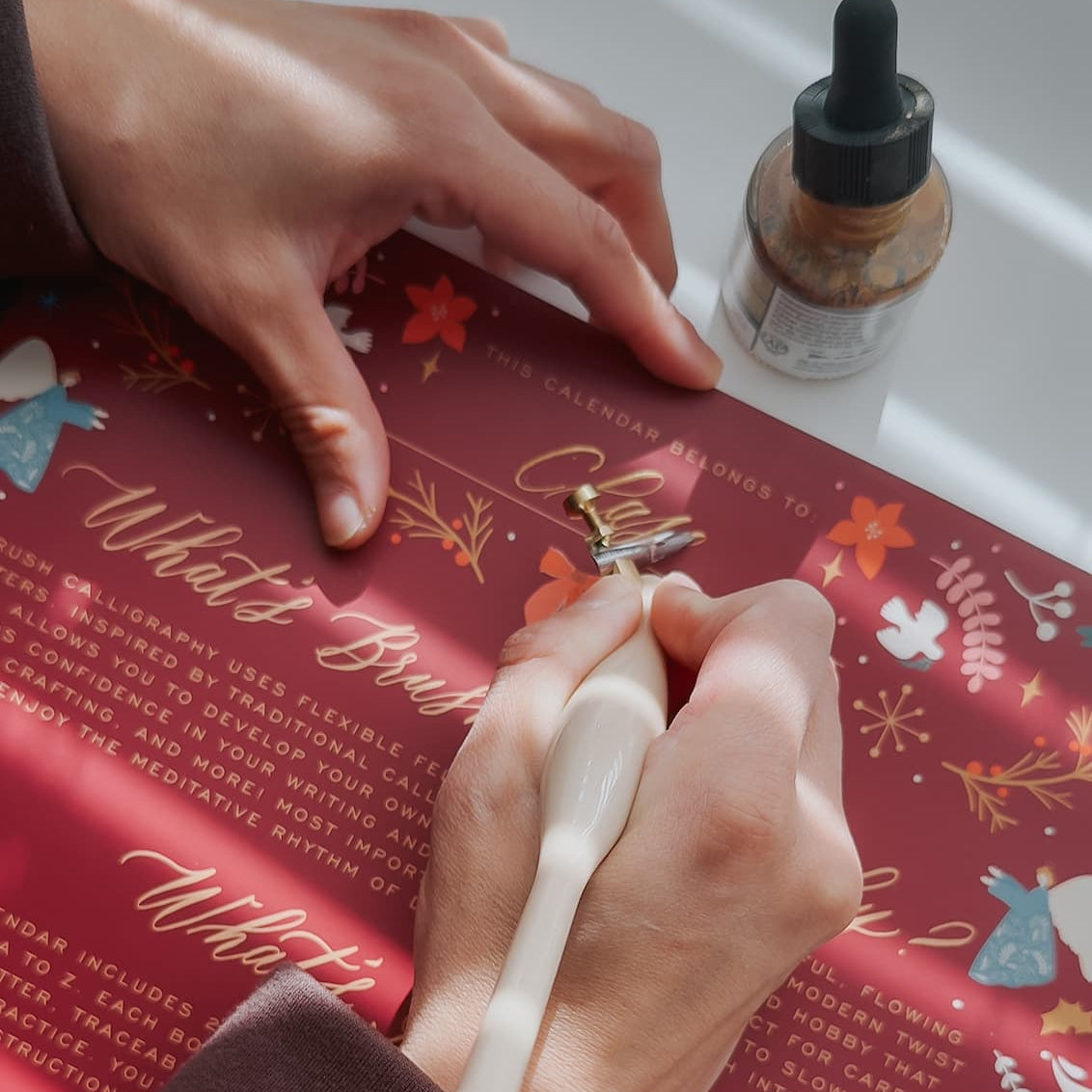 Karla personalizing the Brush Calligraphy Advent Calendar with gold ink using a beige calligraphy pen.
