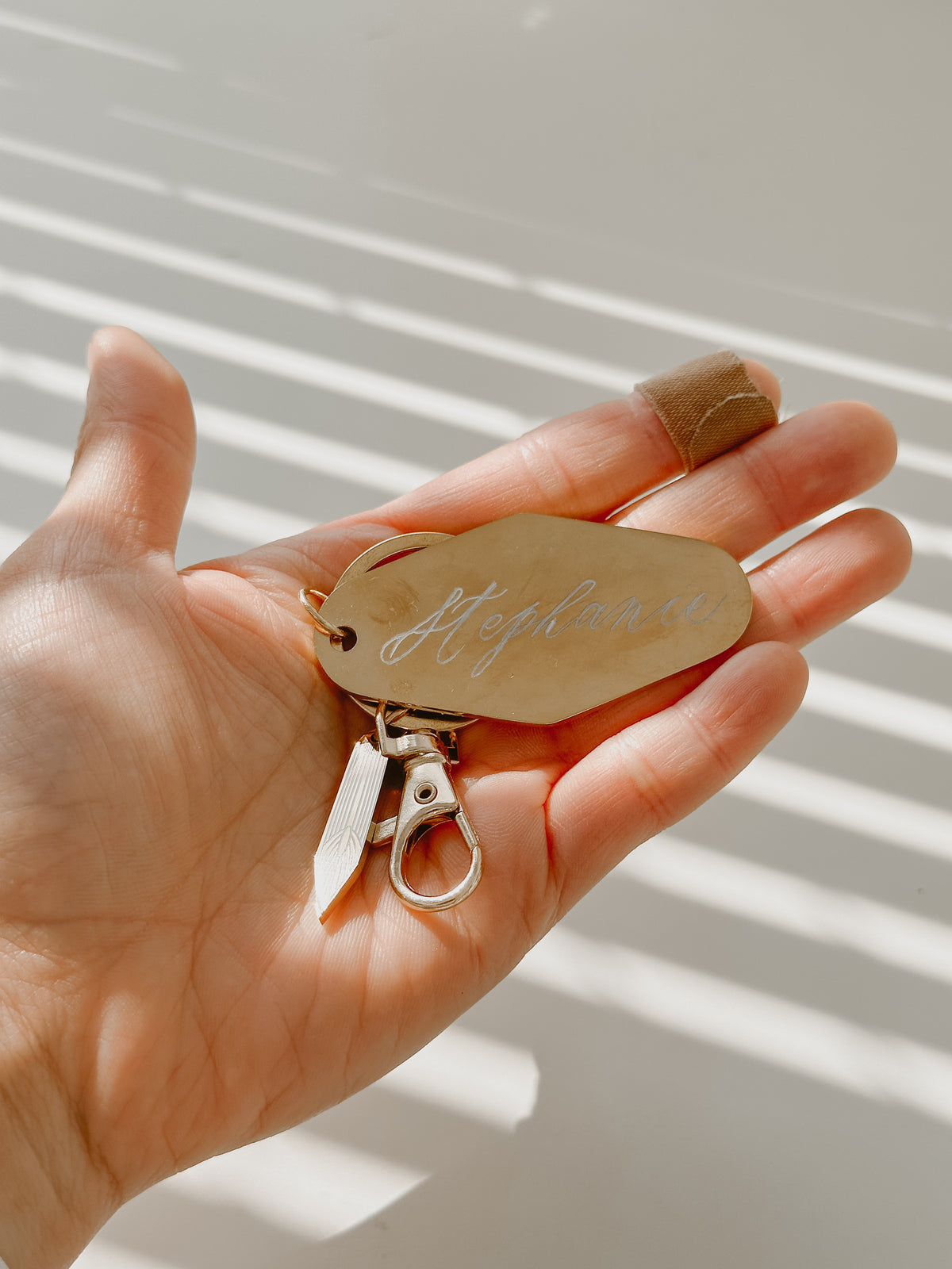 Personalized metal motel keychain with custom calligraphy name engraving, gold key ring, and calligraphy nib charm, shown in hand for size reference and everyday use.