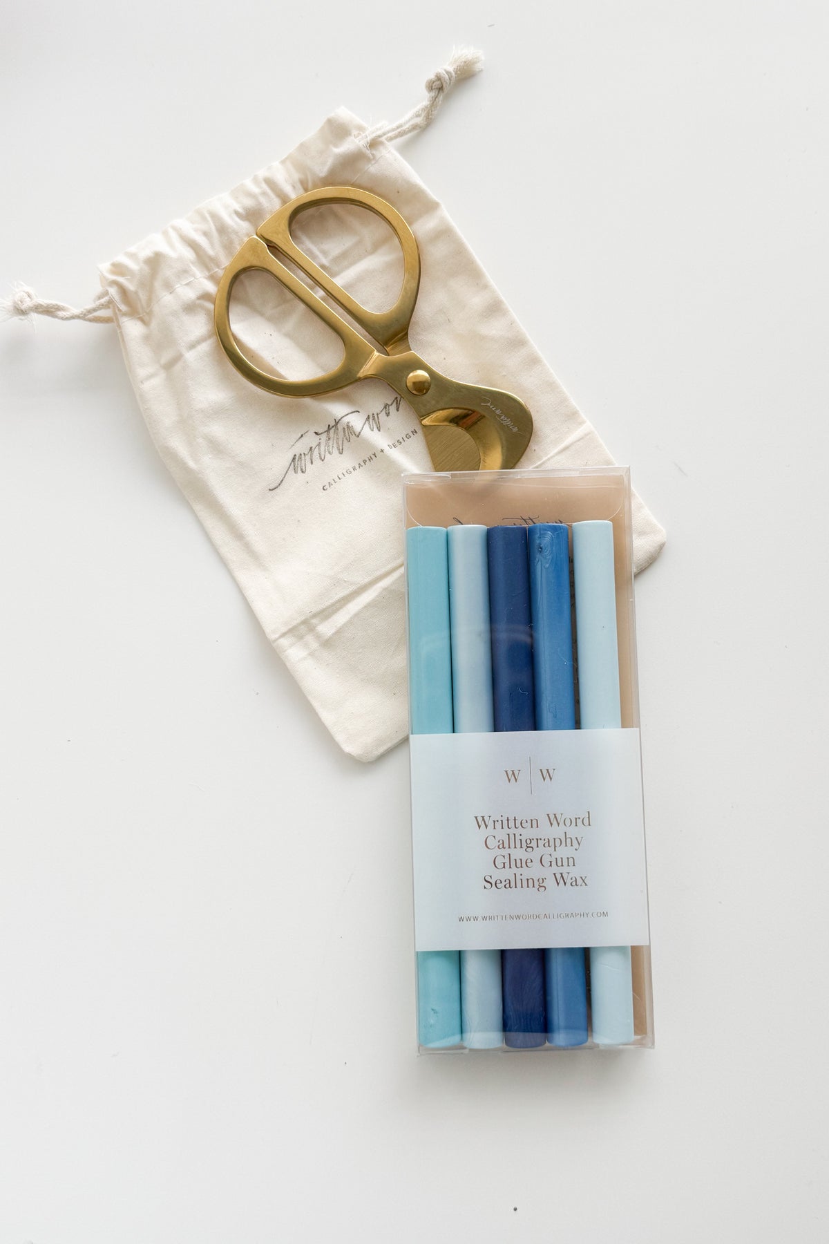 Gold brass wax cutter with a cotton storage pouch beside blue gradient glue gun sealing wax sticks for creating custom wax seals on wedding invitations, envelopes, and stationery.