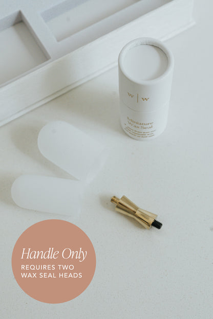 White cylindrical container next to a gold mini wax seal handle on a light surface, with text indicating 'Handle Only' and 'Requires Two Wax Seal Heads'.