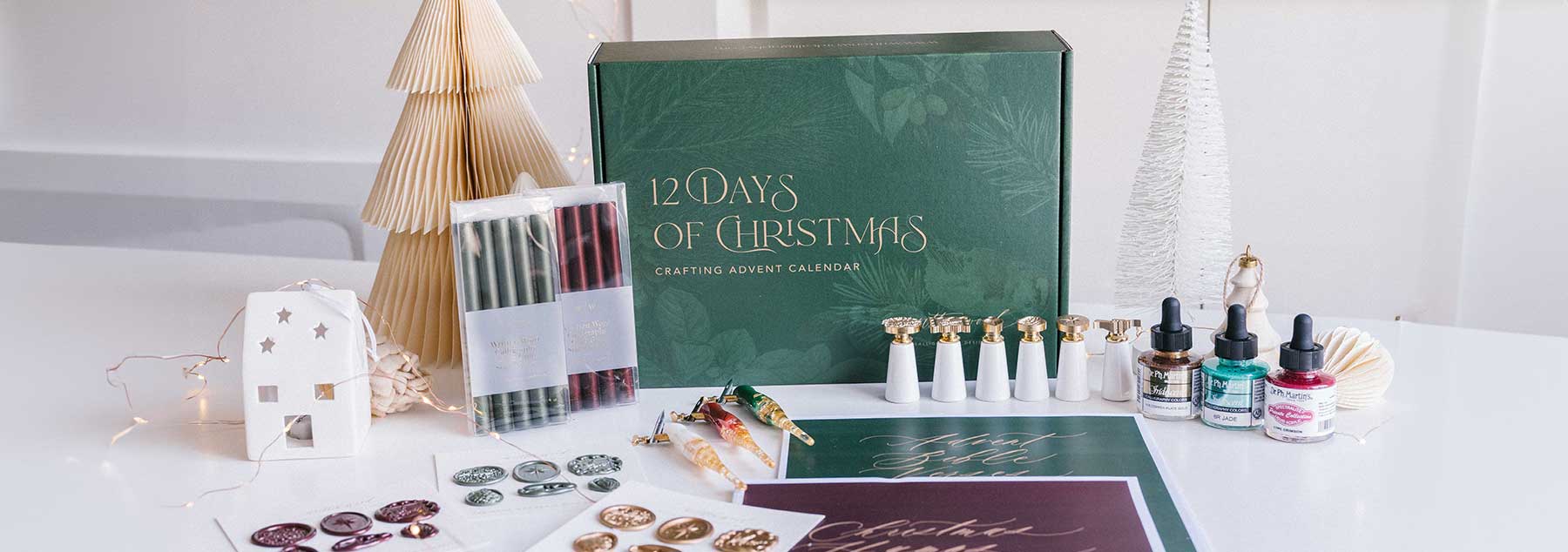 Holiday crafting advent calendar featuring wax seal stamps, sealing wax, calligraphy penholders, inks, and festive creative supplies arranged in a Christmas-inspired display.