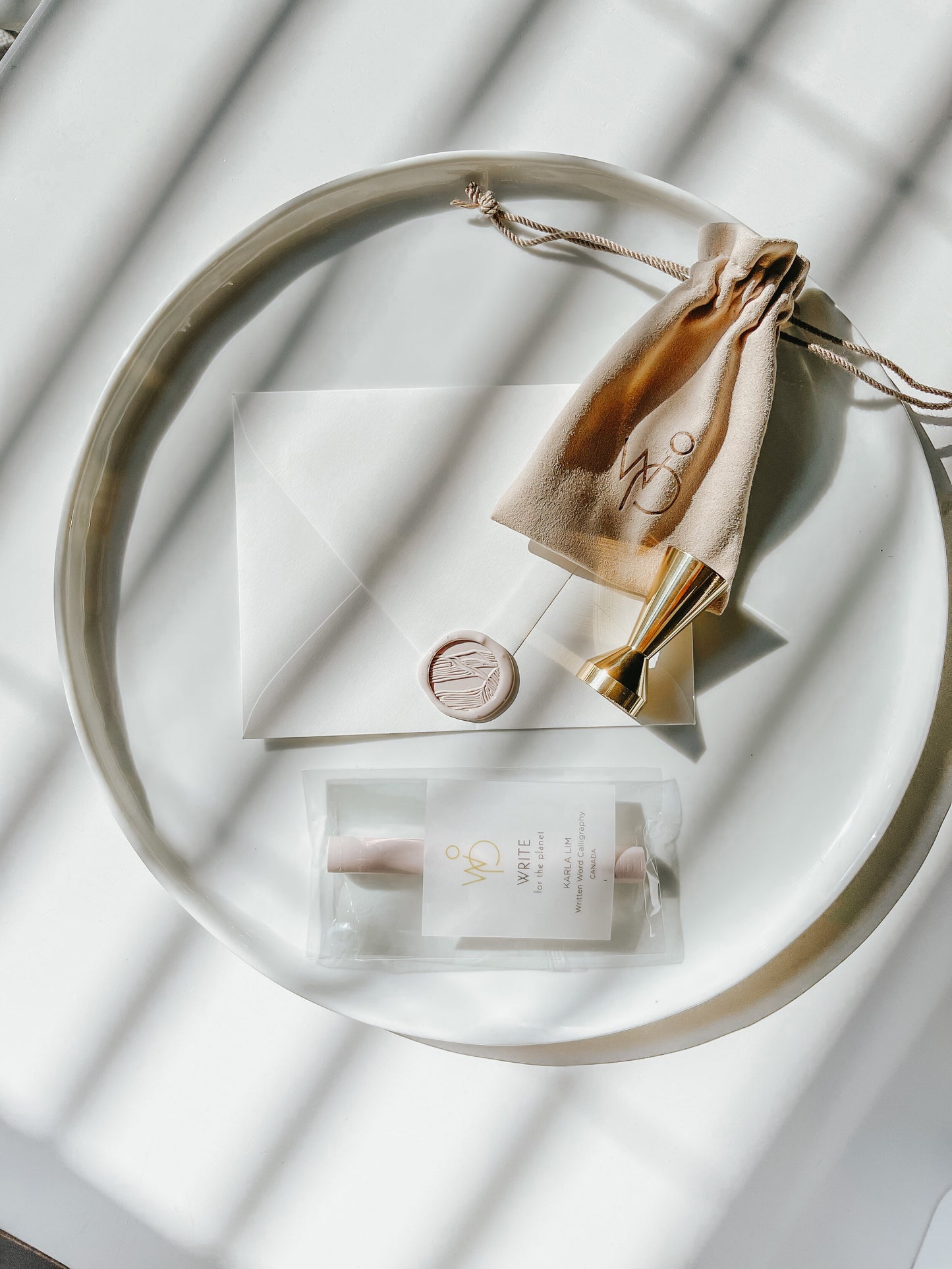 Sand dunes wax seal stamp with a blush wax seal on an envelope, gold brass stamp, and sealing wax set, styled on a white tray
