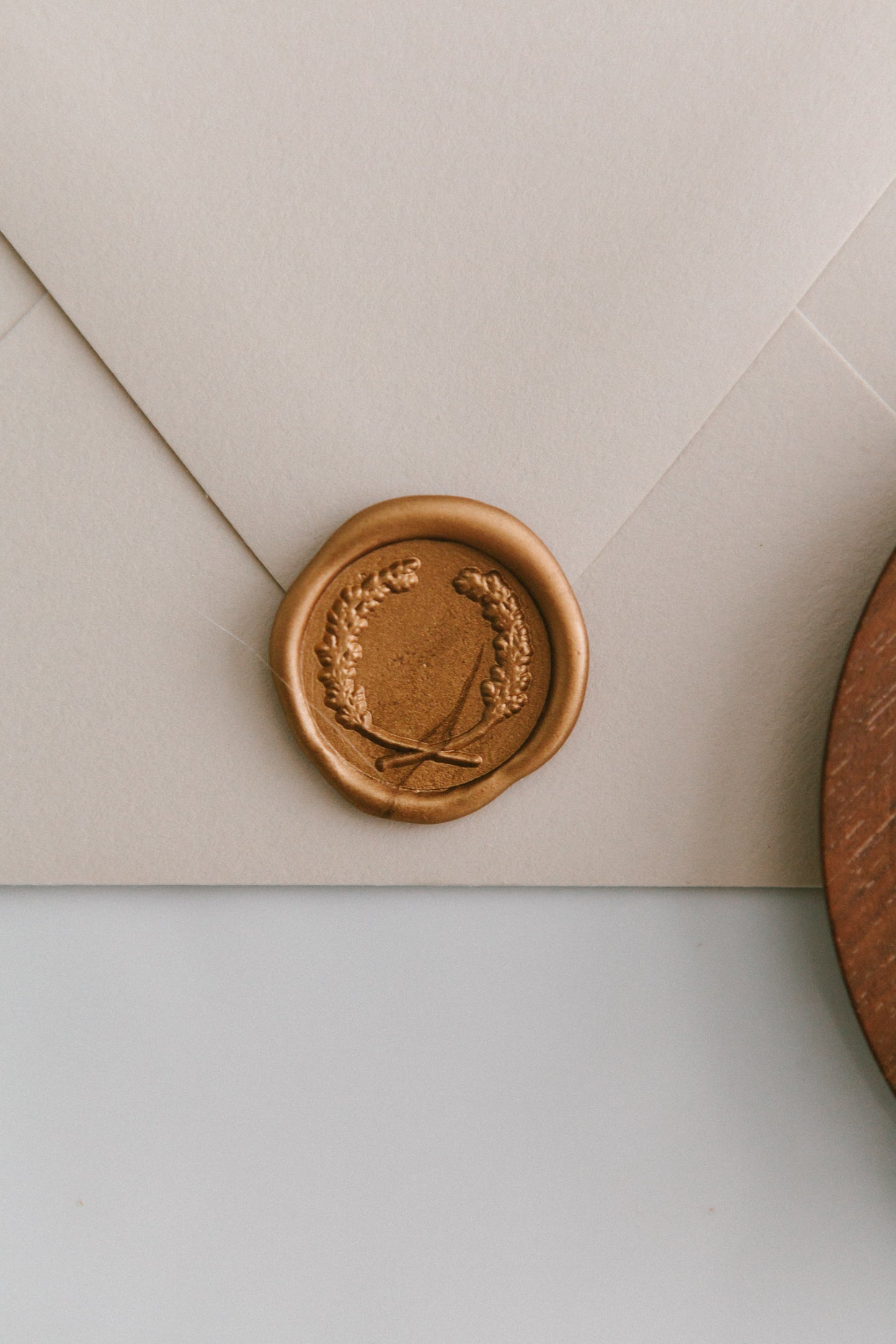 A close-up of a golden laurel crest wax seal, styled on a beige sealed envelope on a white surface