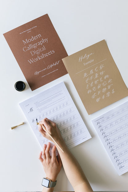 Modern calligraphy digital worksheets with uppercase alphabet and Halcyon exemplar sheet on desk