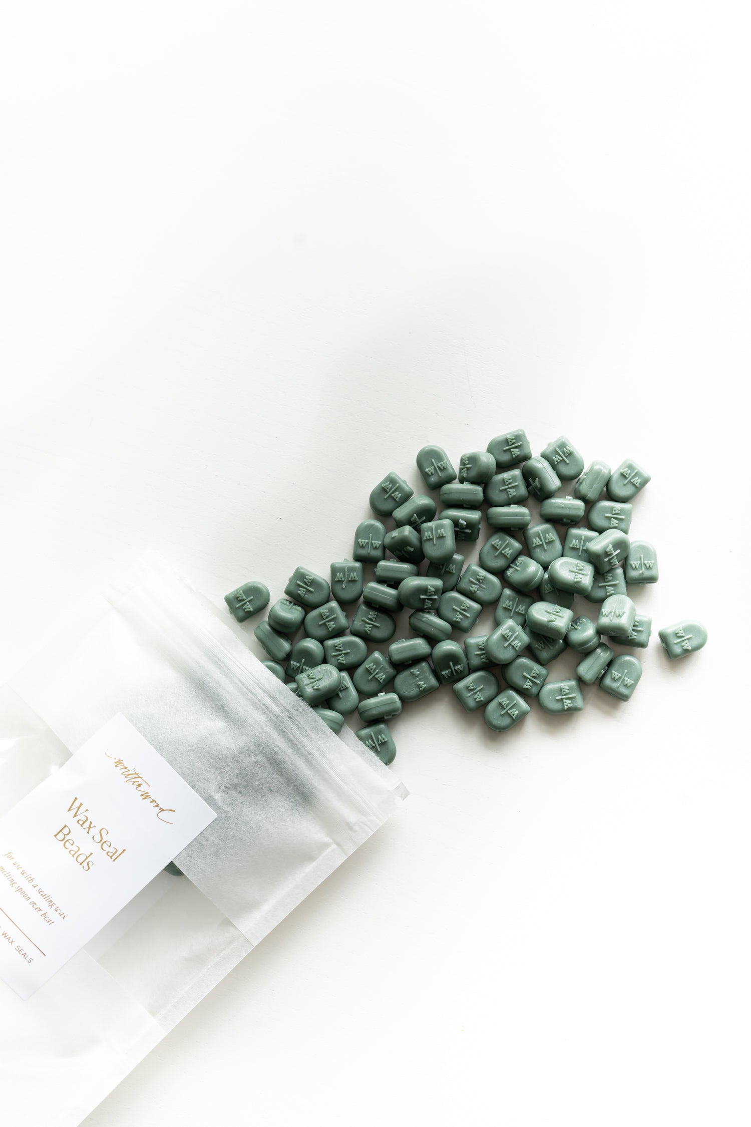 Forest green sealing wax beads spilled from pouch on white background