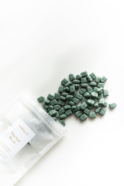 Forest green sealing wax beads spilled from pouch on white background