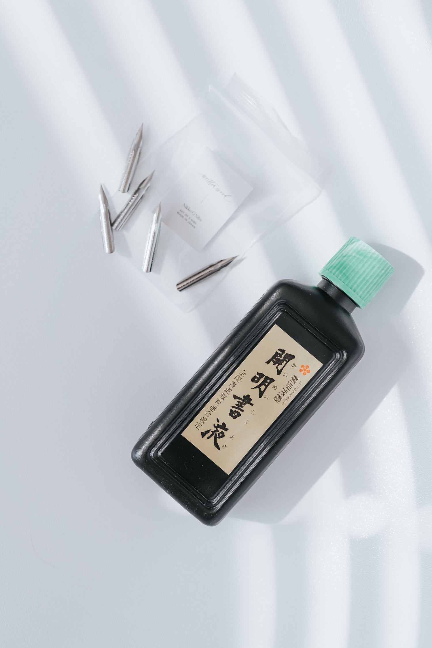 Nikko G calligraphy nibs in a clear bag with a bottle of ink on a white background with soft shadows