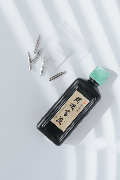 Nikko G calligraphy nibs in a clear bag with a bottle of ink on a white background with soft shadows