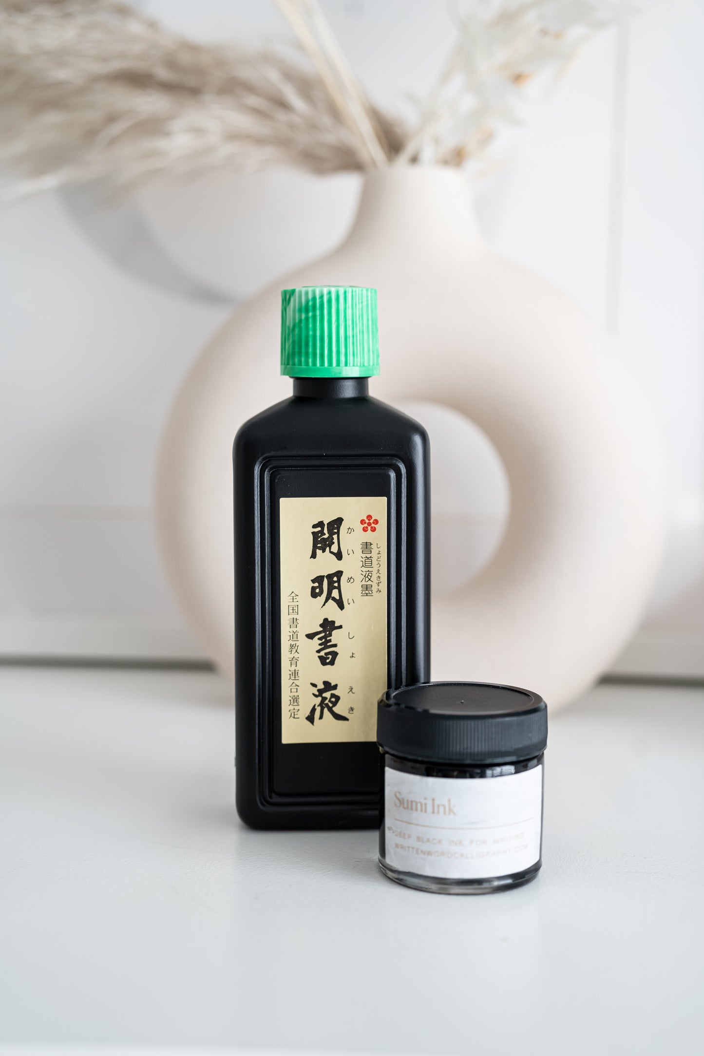 Black Sumi ink bottle and jar with dried flowers and modern vase in the background