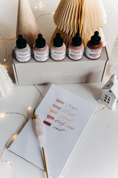 Dr. Ph. Martin's Warm Tone Calligraphy Ink Set displayed with swatches, dip pen, and festive decor on a desk