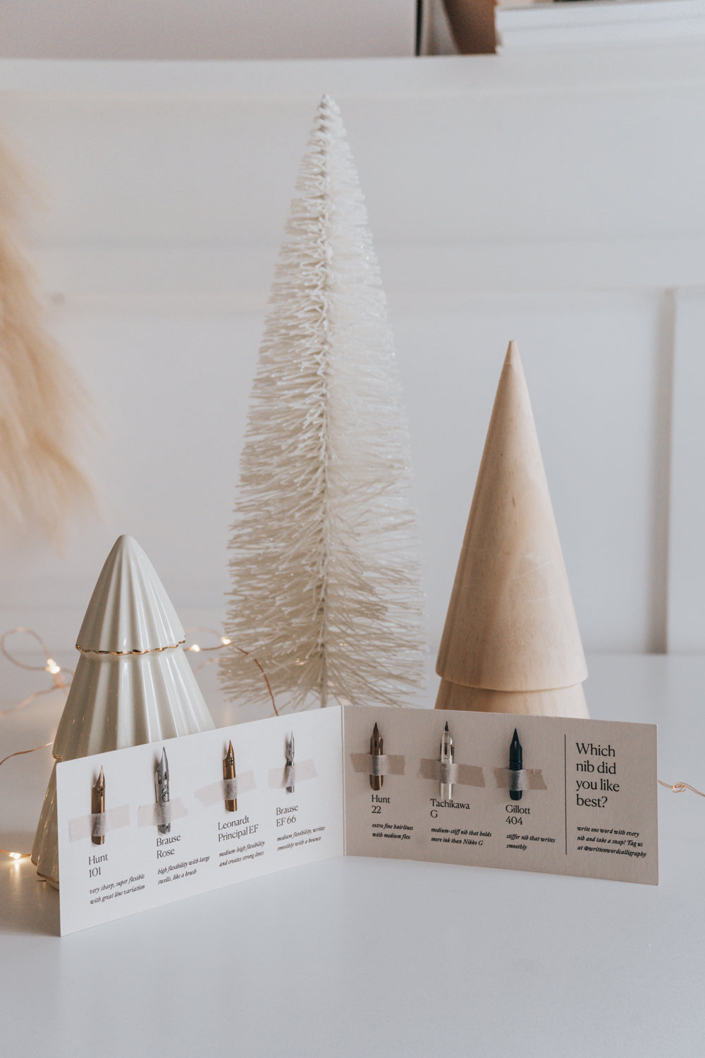 A selection of 7 calligraphy nibs displayed in a booklet next to white holiday trees