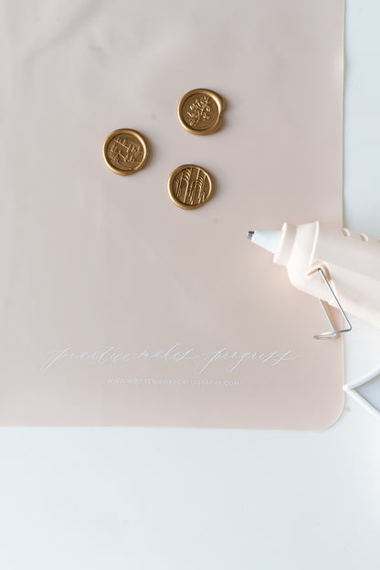 A pink silicone practice mat with three wax seals and a glue gun on top, with 'practice makes progress' in white
