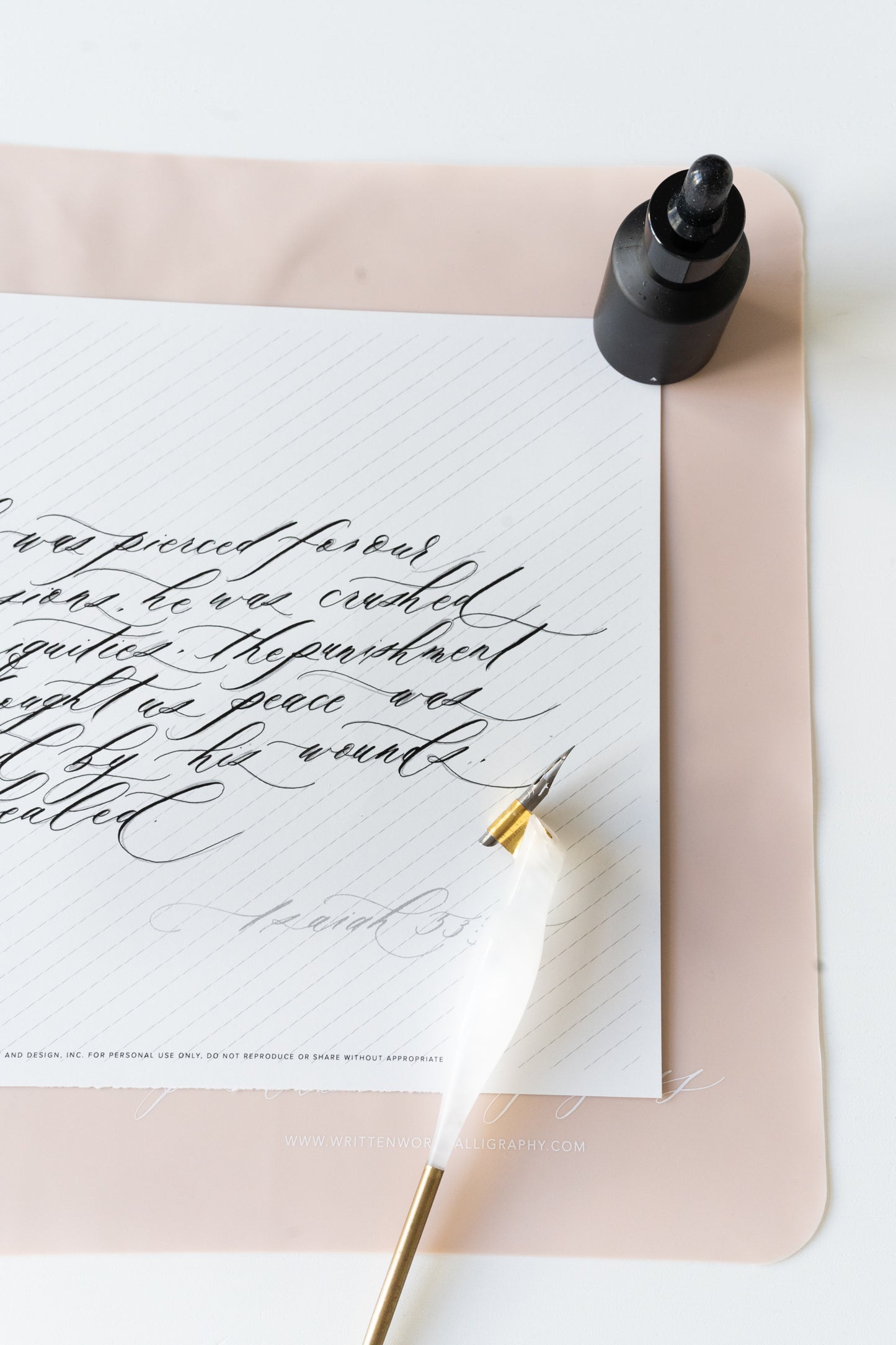 calligraphy pen rests on a slanted grid notepad with ink bottle and a pink silicone mat with 'practice makes progress' text