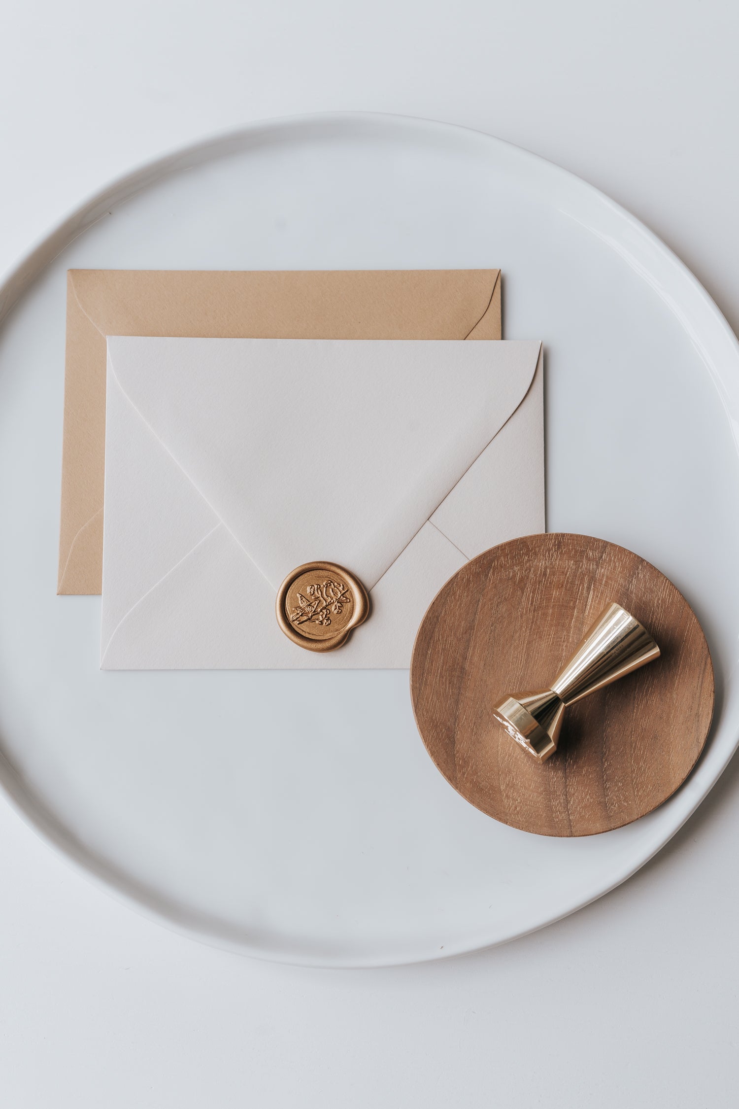 Brass wax seal stamp on a wooden dish beside envelopes with a gold birds wax seal, styled on a white ceramic plate.