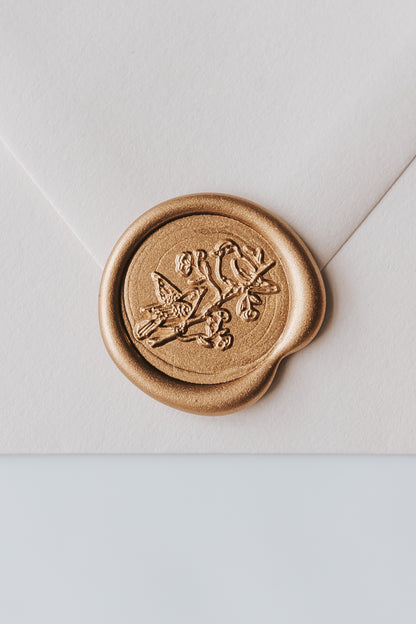 A close-up of a golden birds wax seal, styled on a beige sealed envelope on a white surface