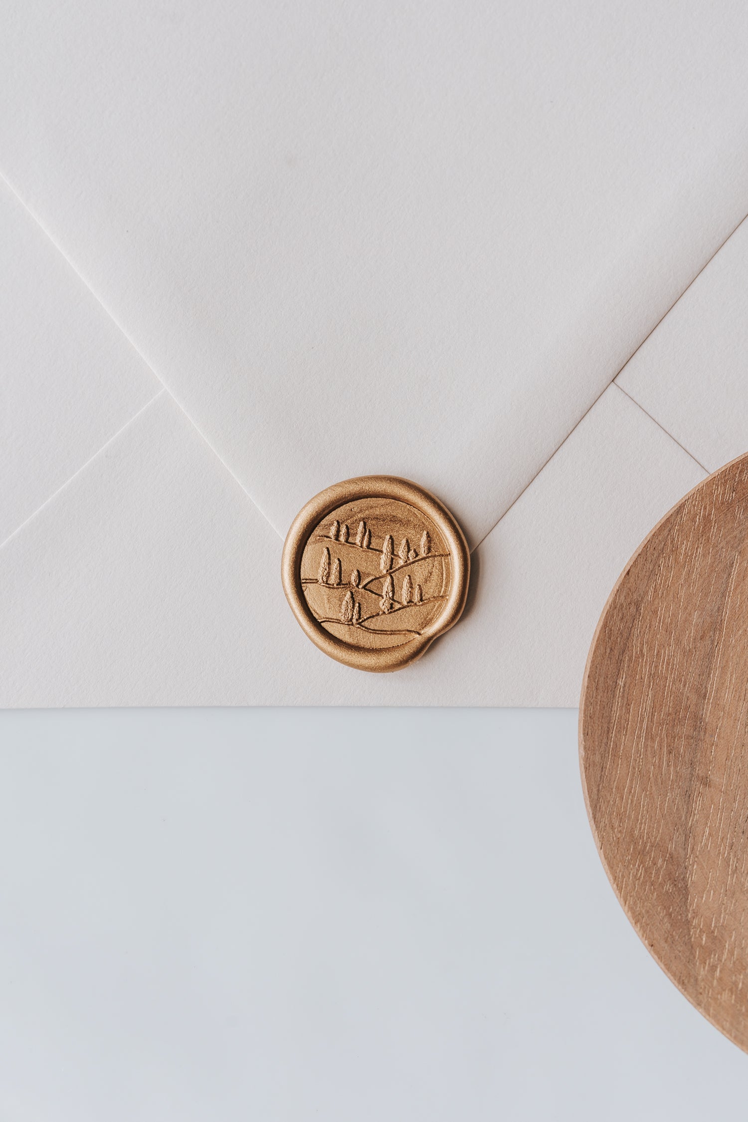 A golden Tuscany wax seal, styled on a beige sealed envelope and a wooden dish on the side