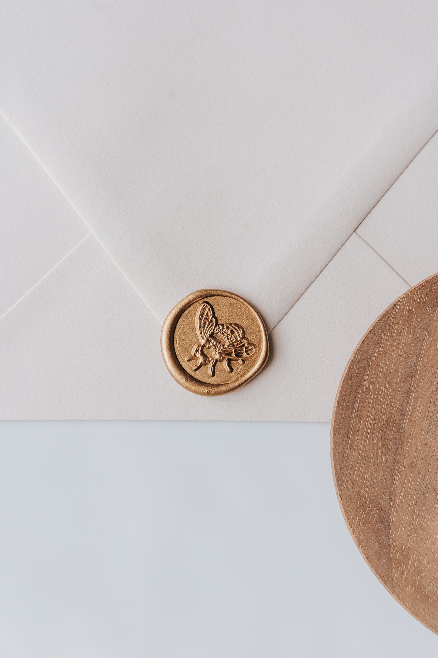 A golden honeybee wax seal, styled on a beige sealed envelope and a wooden dish on the side