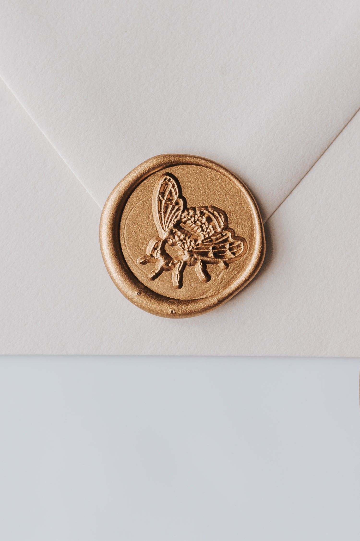 A close-up of a golden honeybee wax seal, styled on a beige sealed envelope on a white surface