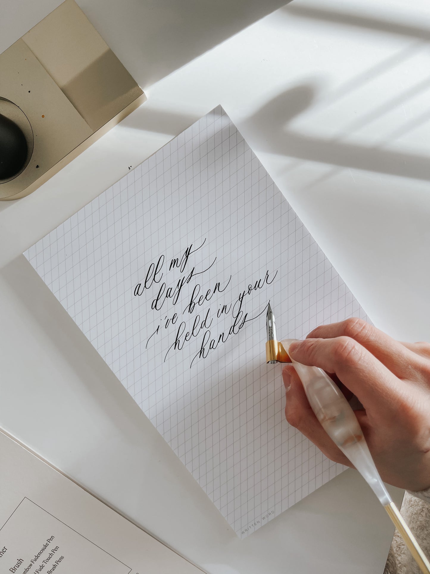 Hand holding a resin calligraphy pen writing on slanted grid notepad with beautiful calligraphy