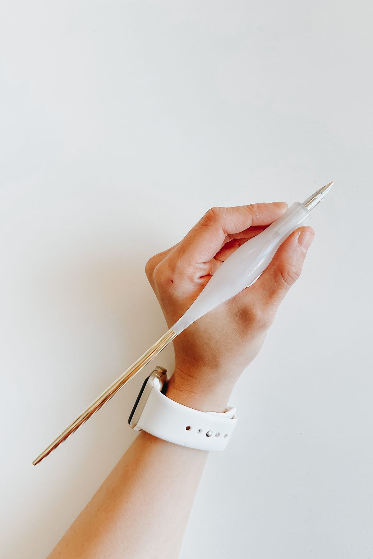 Straight calligraphy pen with a white quartz resin holder and brass tail, held in hand, ideal for various calligraphy nibs