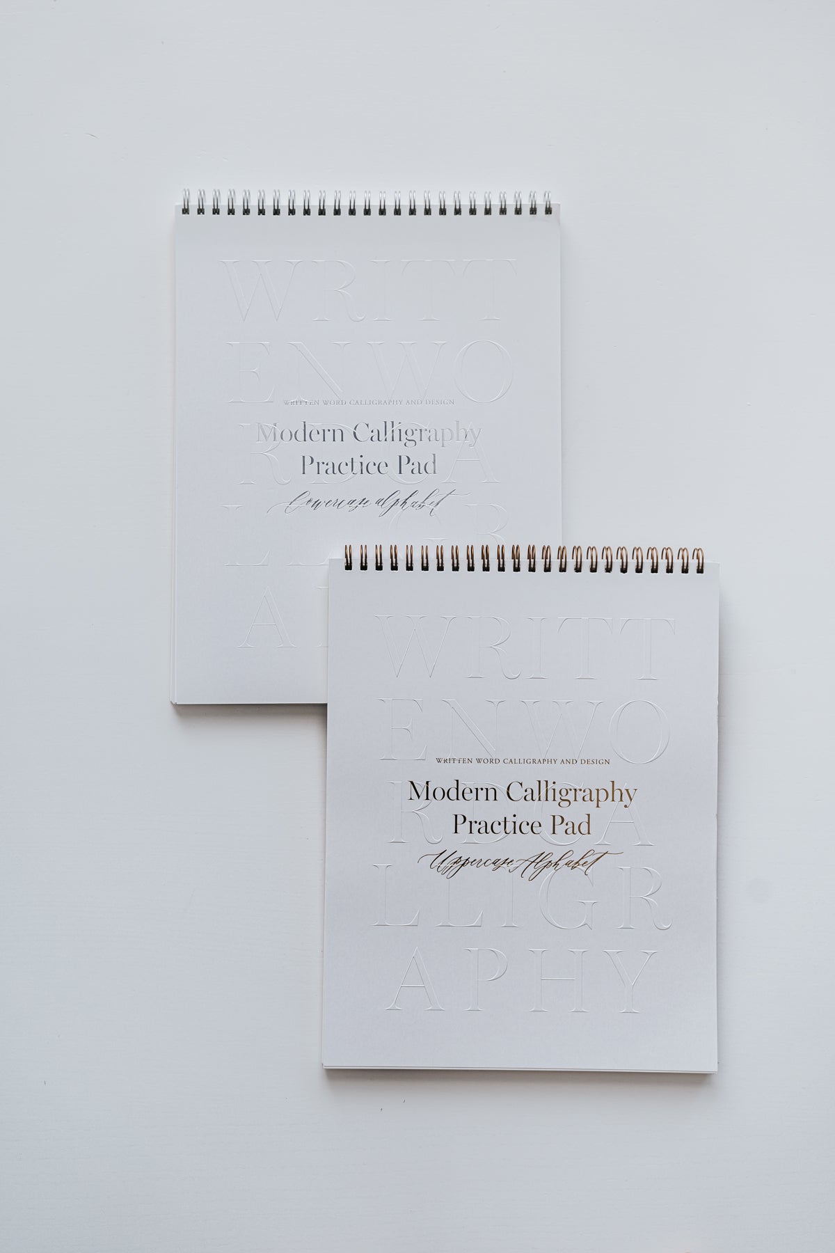 Two modern calligraphy practice pads for uppercase and lowercase alphabets, featuring sleek spiral binding on a white background