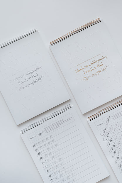 Four modern calligraphy practice pads featuring uppercase and lowercase alphabet exercises, displayed on a white background