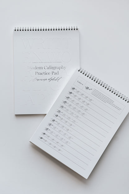 Two spiral-bound modern calligraphy practice pads, one closed and one open to a lowercase 'w' practice page on a white surface