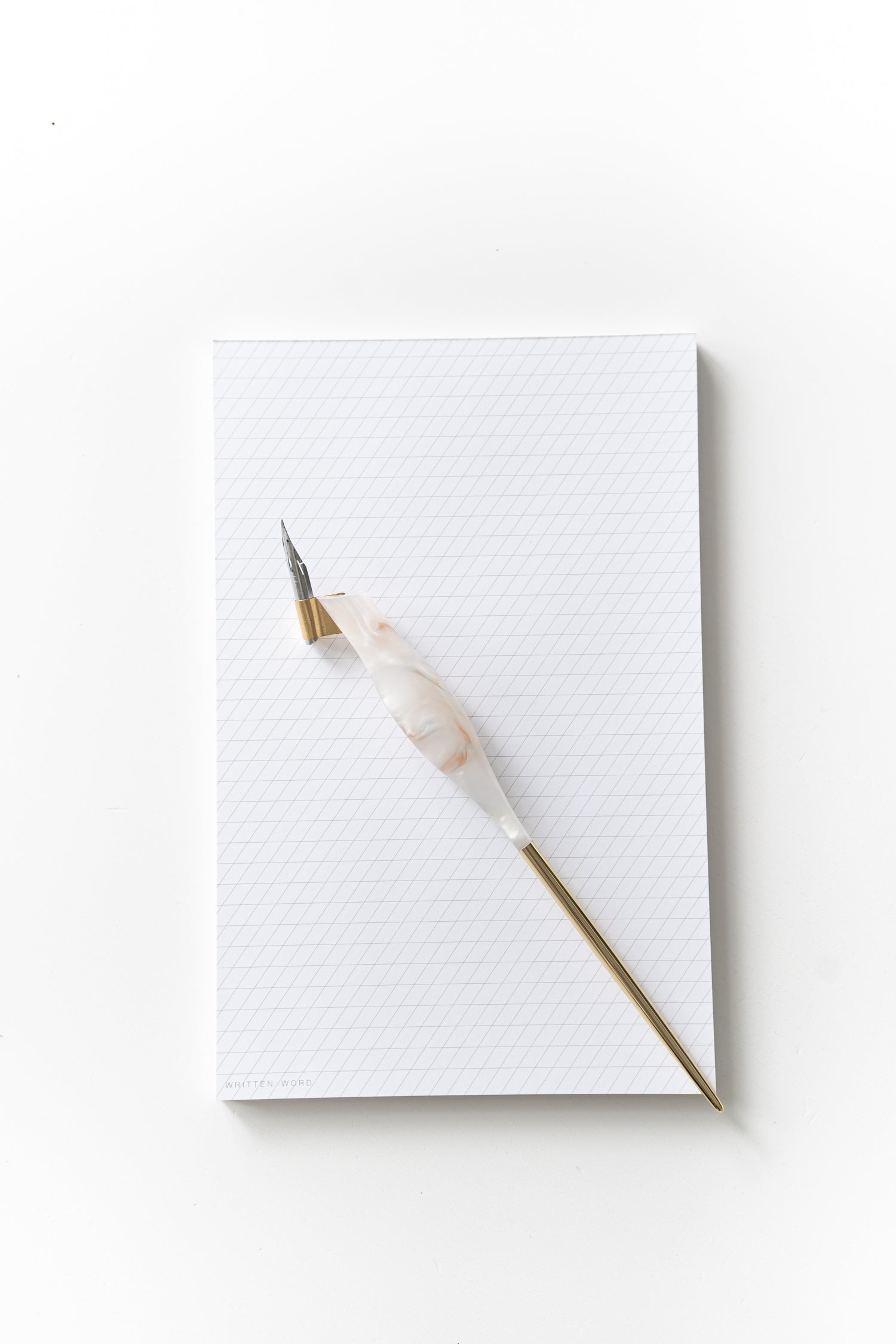 Calligraphy pen resting on a slanted grid notepad, ready for practice with ink-friendly sheets