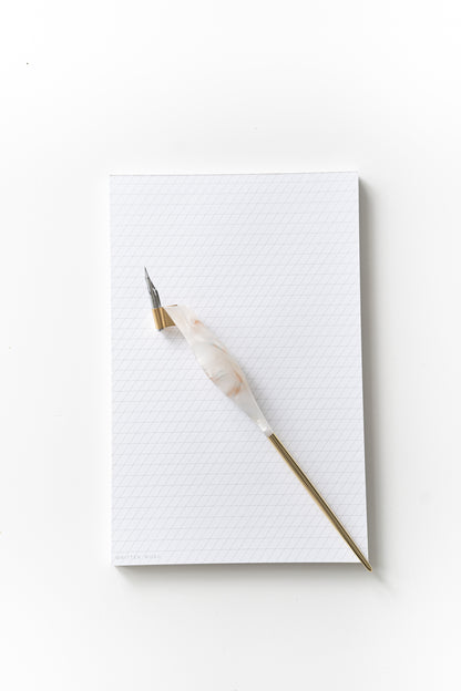 Calligraphy pen resting on a slanted grid notepad, ready for practice with ink-friendly sheets