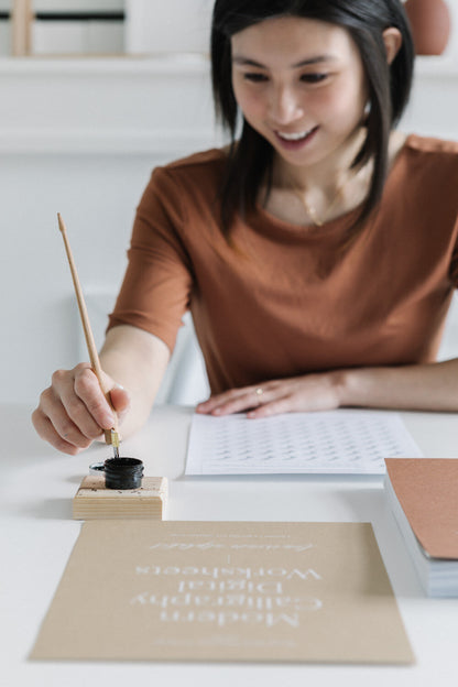Karla practicing modern calligraphy with dip pen and ink using printable worksheets at desk