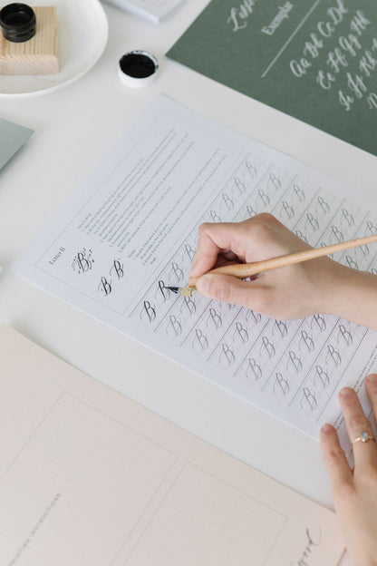 Close-up of writing uppercase B in modern calligraphy using dip pen on practice worksheet