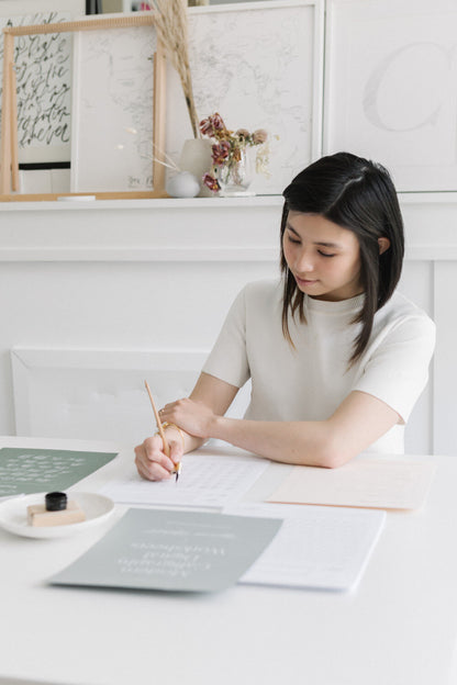 Karla practicing modern calligraphy with dip pen and printable worksheets at clean desk