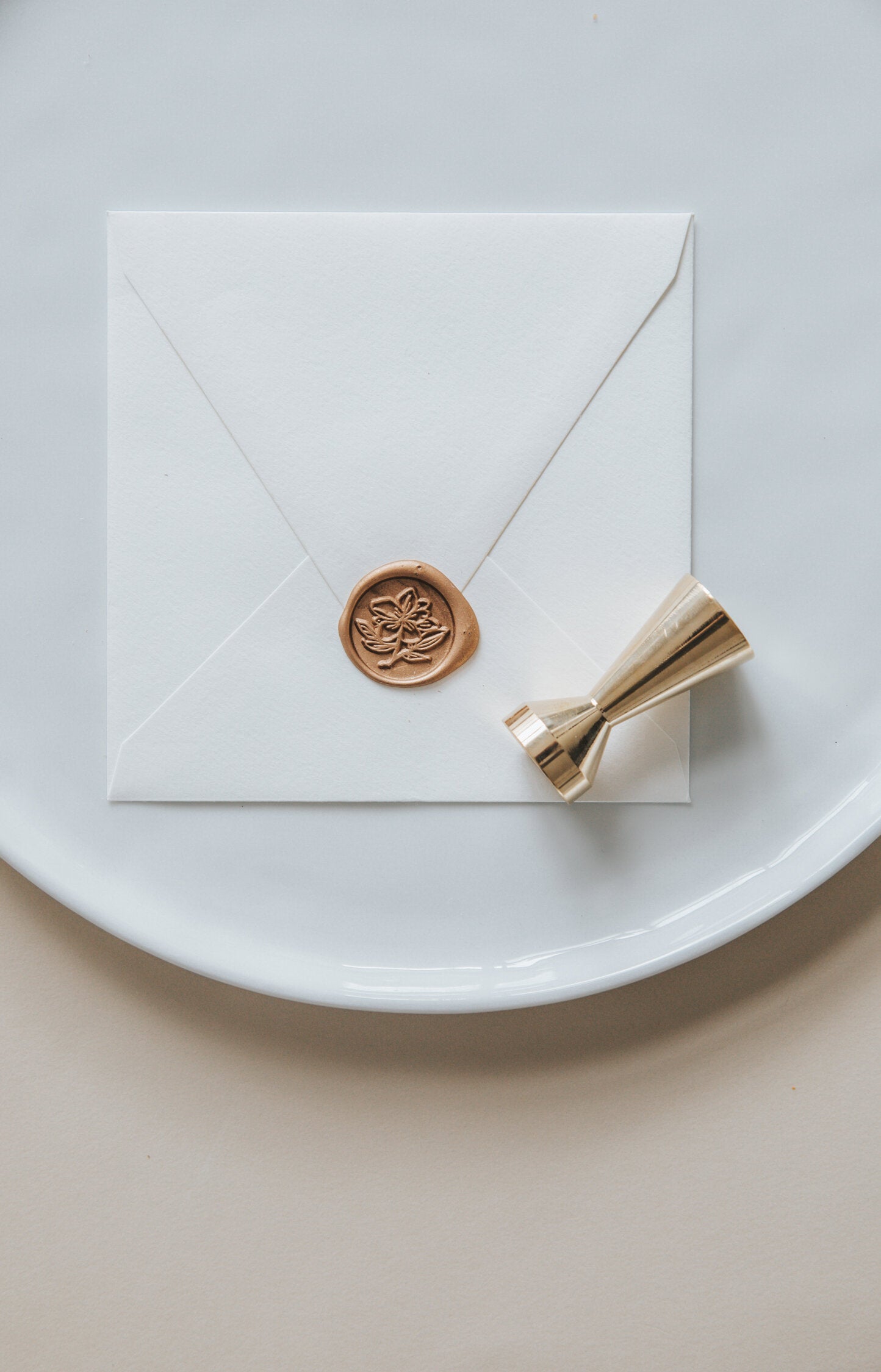 A golden magnolia wax seal, styled on a white sealed envelope and a brass wax seal stamp on the side