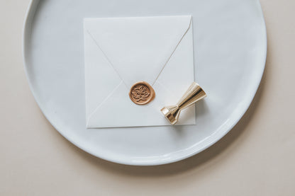 A golden magnolia wax seal, styled on a white sealed envelope and a brass wax seal stamp on the side