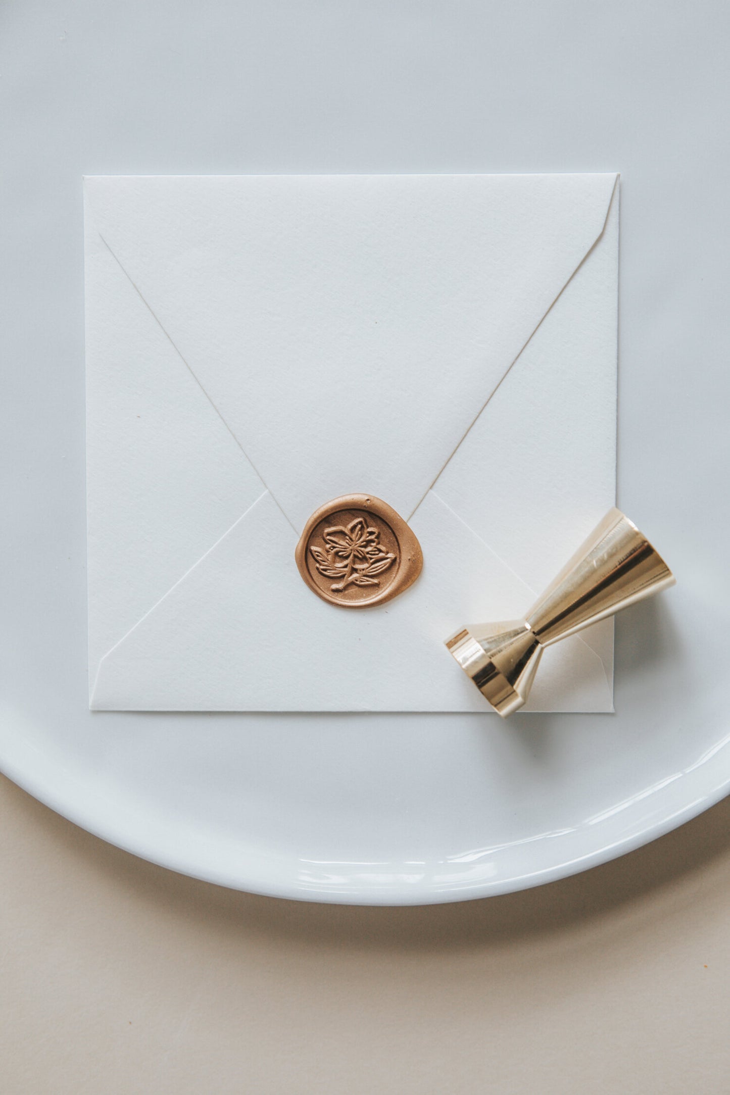 A golden magnolia wax seal, styled on a white sealed envelope and a brass wax seal stamp on the side