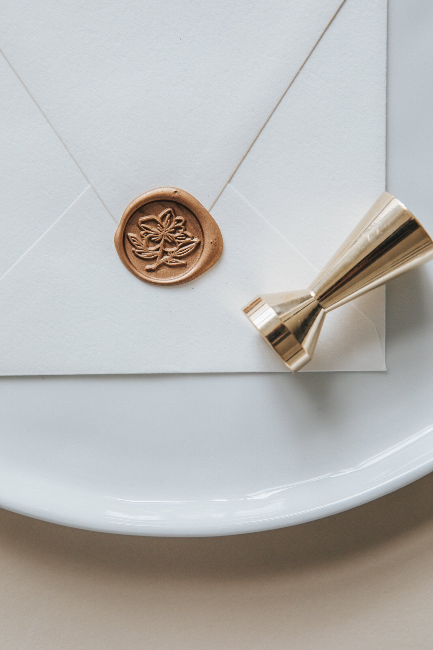 A close-up of a gold magnolia wax seal, styled on a white sealed envelope and a brass wax seal stamp on the side
