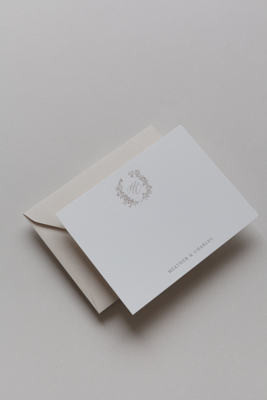 Custom stationery card with gold monogram wreath and envelope in soft neutral tones