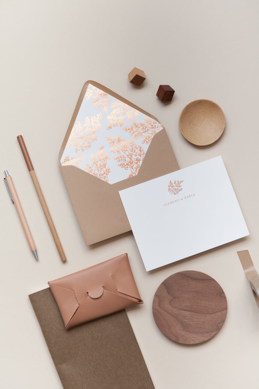 Flat lay of personalized card and envelope with floral liner and warm neutral desk accessories